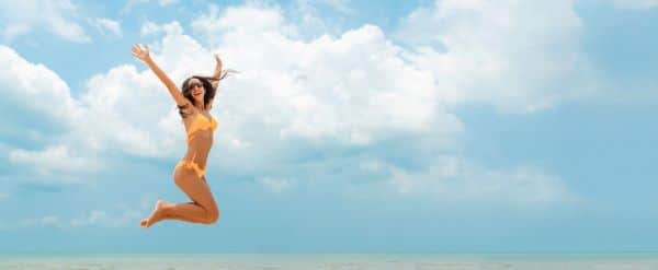 Mulher, na beira da praia, saltando para foto frente ao mar.