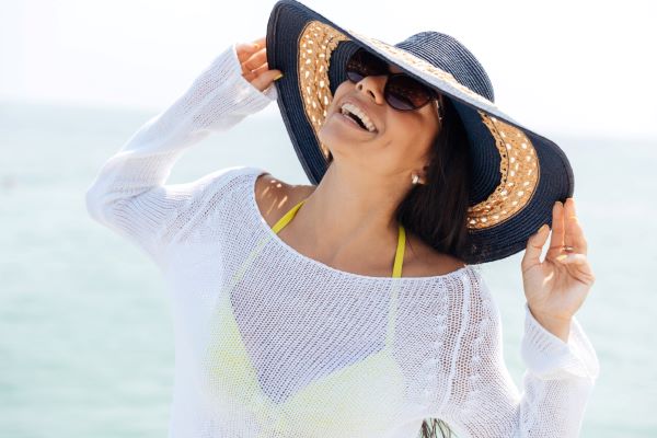Mulher com óculos e chapéu protegendo o rosto dos raios UV.