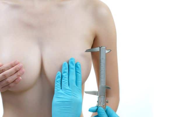 Médico medindo o grau de flacidez mamária, nos seios da paciente, antes da realização da mastopexia.